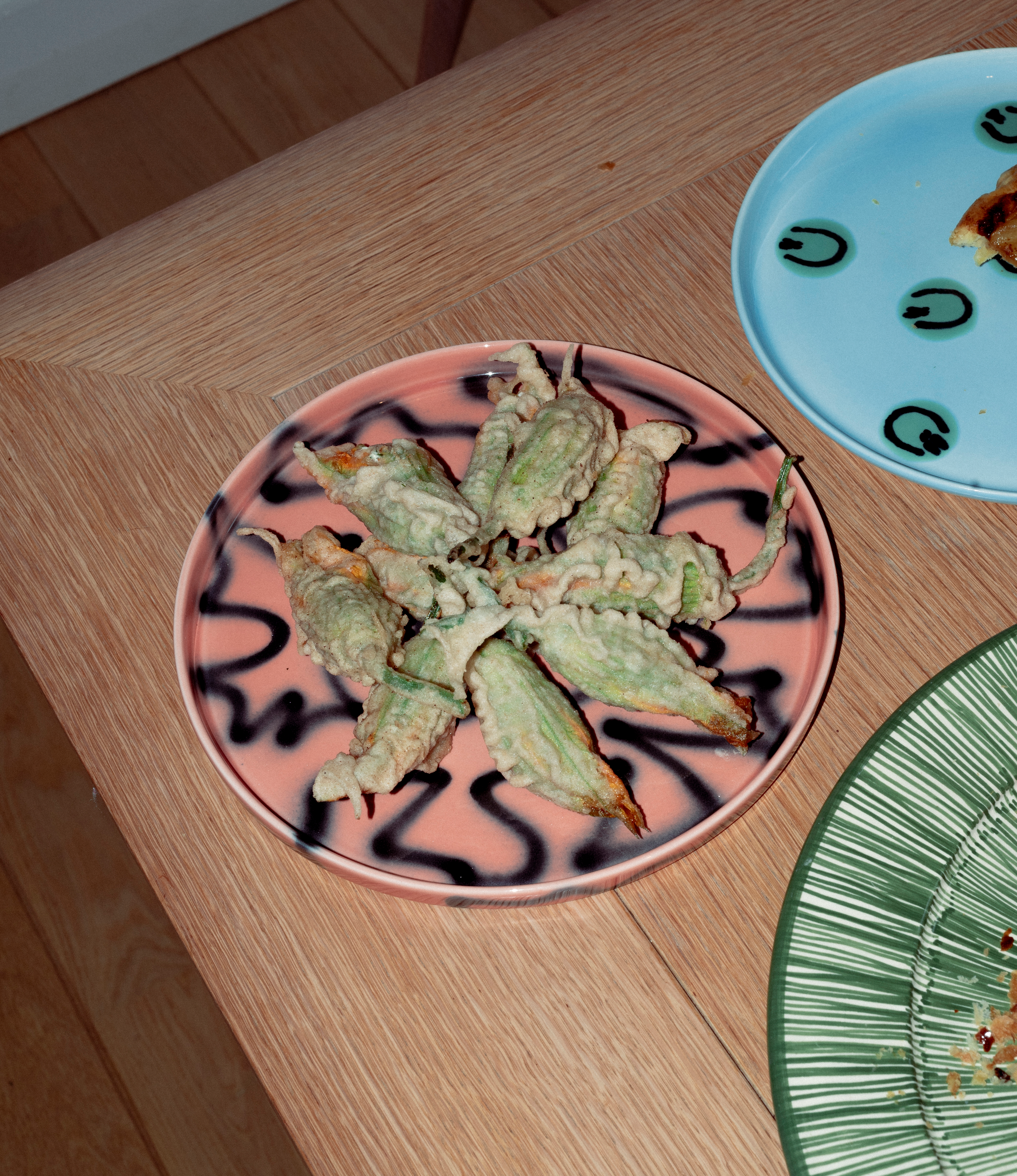 Peach Pizza Tray from Frizbee Ceramics. The tray is coming in the soothing peach color matched with the contrasting black zig-zag pattern. The plate is holding stuffed, fried zucchini flowers.